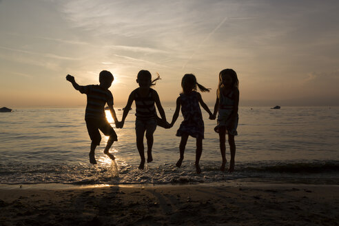 Italy, Lake Garda, children jumping on beach at sunset - SARF000842