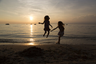 Italien, Gardasee, zwei Mädchen springen bei Sonnenuntergang am Strand - SARF000843