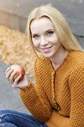 Portrait of smiling young woman holding an apple wearing cardigan - GDF000451