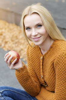 Porträt einer lächelnden jungen Frau, die einen Apfel hält und eine Strickjacke trägt - GDF000451
