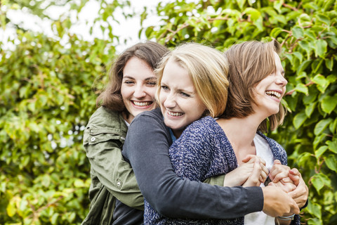 Drei Freundinnen umarmen sich im Garten, lizenzfreies Stockfoto