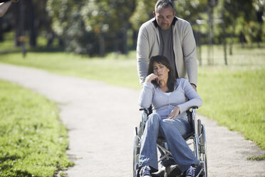 Man pushing woman in wheelchair in park - ZEF000408