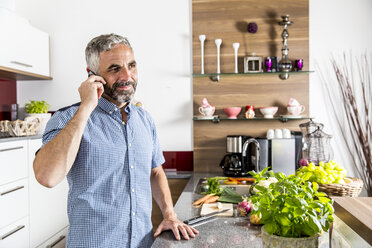 Austria, Man in kitchen using smart phone - MBEF001235