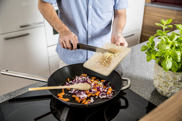 Österreich, Mann in der Küche, der Knoblauch in die Pfanne gibt - MBEF001237