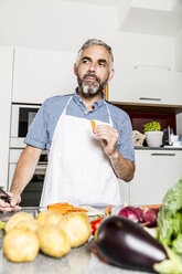 Austria, Man in kitchen eating carrot - MBEF001246