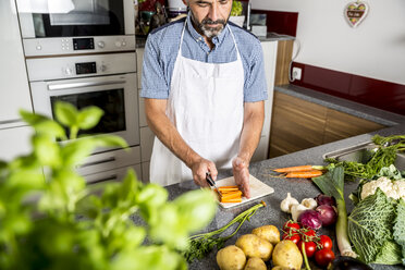 Austria, Man in kitchen chopping carrots - MBEF001247