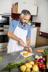 Austria, Man in kitchen chopping carrots - MBEF001248