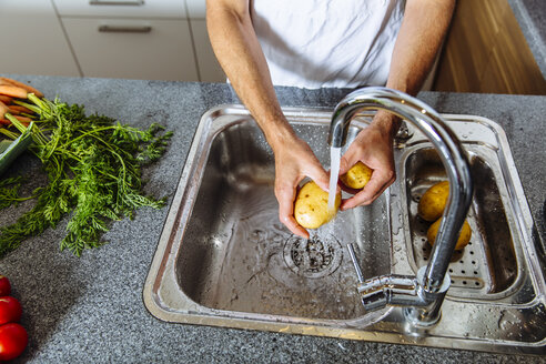 Austria, Man in kitchen washing vegetables - MBEF001251