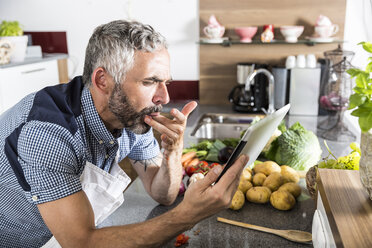 Austria, Man in kitchen holding digital tablet, looking for recipe - MBEF001255