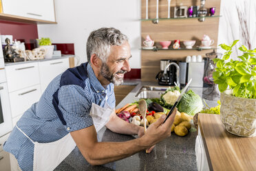 Austria, Man in kitchen holding digital tablet, looking for recipe - MBEF001257