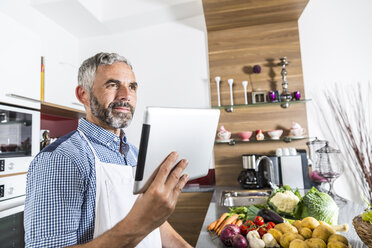 Austria, Man in kitchen holding digital tablet, looking for recipe - MBEF001258