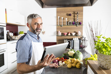 Austria, Man in kitchen holding digital tablet, looking for recipe - MBEF001260