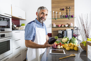 Austria, Man in kitchen with digital tablet preparing food - MBEF001261