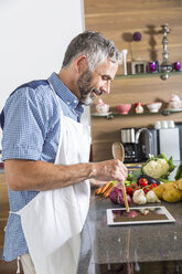 Austria, Man in kitchen with digital tablet preparing food - MBEF001262