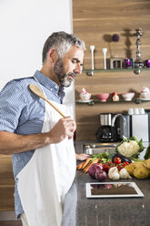 Austria, Man in kitchen with digital tablet preparing food - MBEF001263