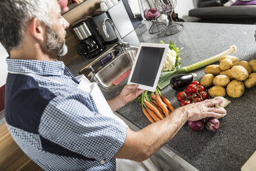 Austria, Man in kitchen with digital tablet preparing food - MBEF001264