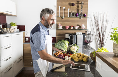 Austria, Man in kitchen with digital tablet preparing food - MBEF001267