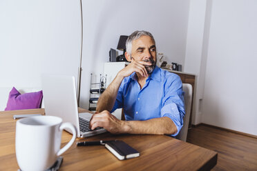 Nachdenklicher Geschäftsmann bei der Arbeit mit dem Laptop im Home Office - MBEF001307