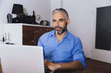 Porträt eines Geschäftsmannes, der im Büro zu Hause mit einem Laptop arbeitet - MBEF001181