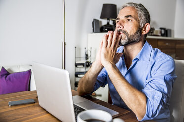 Portrait of pansive businessman working with laptop at home office - MBEF001287