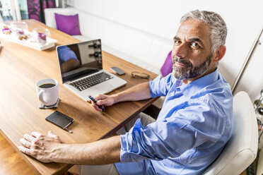 Portrait of businessman with laptop at his home office - MBEF001288