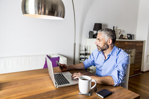 Porträt eines Geschäftsmannes, der im Büro zu Hause mit einem Laptop arbeitet - MBEF001308