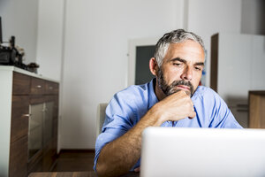 Porträt eines Geschäftsmannes, der im Büro zu Hause mit einem Laptop arbeitet - MBEF001182