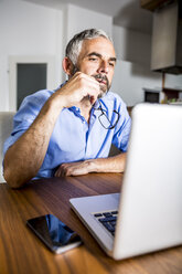 Nachdenklicher Geschäftsmann bei der Arbeit mit dem Laptop im Home Office - MBEF001289