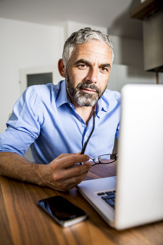 Porträt eines Geschäftsmannes, der im Büro zu Hause mit einem Laptop arbeitet, lizenzfreies Stockfoto