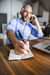 Geschäftsmann, der mit seinem Smartphone telefoniert und sich Notizen macht - MBEF001295