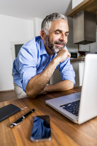 Porträt eines lächelnden Geschäftsmannes im Büro zu Hause, der auf seinen Laptop schaut, lizenzfreies Stockfoto