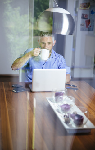 Geschäftsmann arbeitet mit Laptop im Büro zu Hause und trinkt Kaffee, lizenzfreies Stockfoto