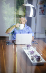 Geschäftsmann arbeitet mit Laptop im Büro zu Hause und trinkt Kaffee - MBEF001185