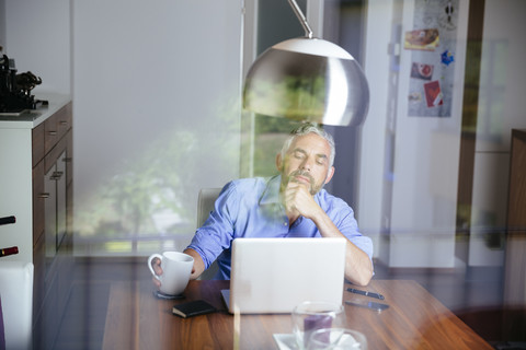 Nachdenklicher Geschäftsmann bei der Arbeit mit dem Laptop im Home Office, lizenzfreies Stockfoto