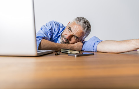 Müder Geschäftsmann mit Laptop im Heimbüro, lizenzfreies Stockfoto