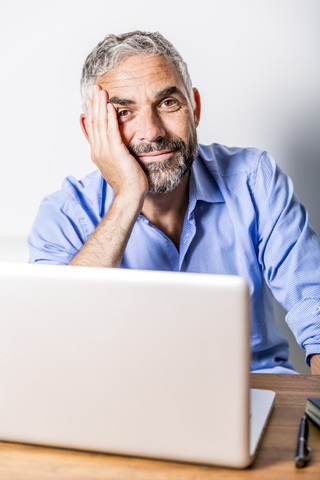 Potrait eines lächelnden Geschäftsmannes mit Laptop in seinem Heimbüro, lizenzfreies Stockfoto