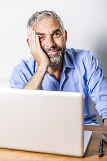 Potrait eines lächelnden Geschäftsmannes mit Laptop in seinem Heimbüro - MBEF001190