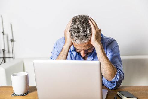 Angry businessman with head in his hands sitting at his home office - MBEF001306