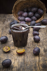 Preserving jar of plum jam and plums on wooden table - LVF001871