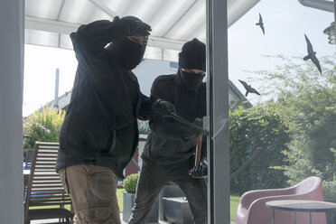 Zwei Einbrecher öffnen zur Tageszeit mit Hammer und Brecheisen die Terrassentür eines Einfamilienhauses - ONF000619