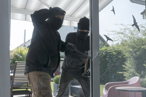 Two burglars opening terrace door of an one-family house with hammer and crowbar at daytime - ONF000619