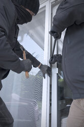 Zwei Einbrecher öffnen die Terrassentür eines Einfamilienhauses mit Hammer und Brecheisen bei Tageslicht, Teilansicht - ONF000621
