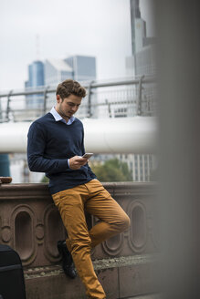 Deutschland, Hessen, Frankfurt, junger Mann steht auf einer Brücke und benutzt sein Smartphone - UUF001815