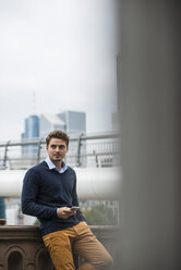 Deutschland, Hessen, Frankfurt, junger Mann steht mit seinem Smartphone auf einer Brücke - UUF001887