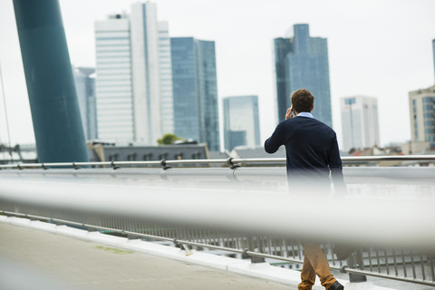 Germany, Hesse, Frankfurt, young businessman walking on a bridge telephoning with his smartphone stock photo