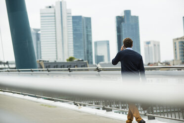 Germany, Hesse, Frankfurt, young businessman walking on a bridge telephoning with his smartphone - UUF001819