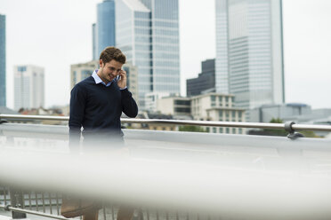 Deutschland, Hessen, Frankfurt, junger Geschäftsmann geht auf einer Brücke und telefoniert mit seinem Smartphone - UUF001820