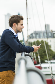 Deutschland, Hessen, Frankfurt, junger Mann auf einer Brücke stehend mit Smartphone in der Hand - UUF001825