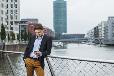 Germany, Hesse, Frankfurt, young businessman standing on a bridge using his smartphone - UUF001830