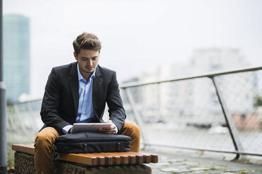 Germany, Hesse, Frankfurt, young man sitting on a bench using his digital tablet - UUF001888